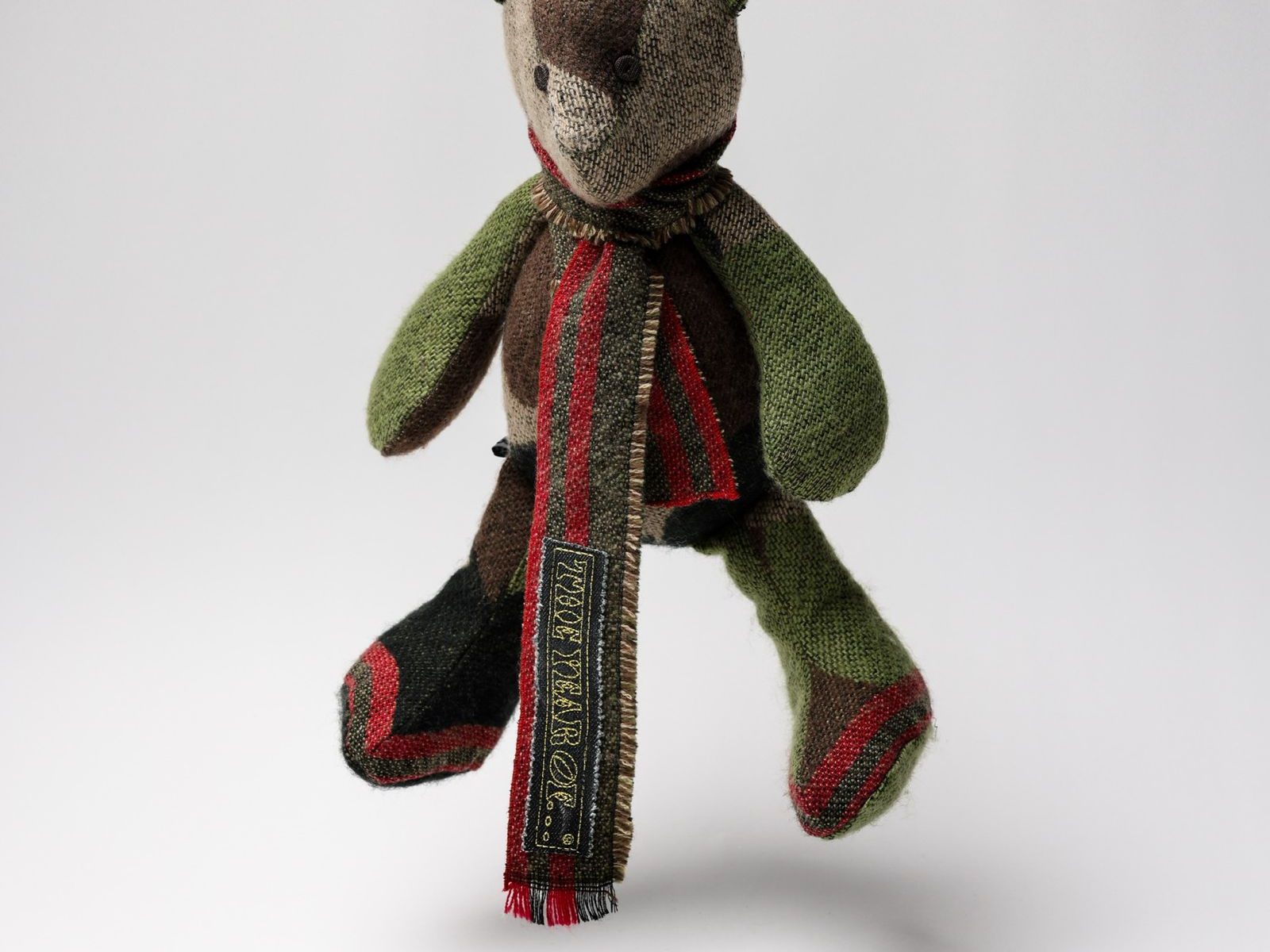 A patchwork tweed teddy bear, its striped scarf carrying The Year of… label